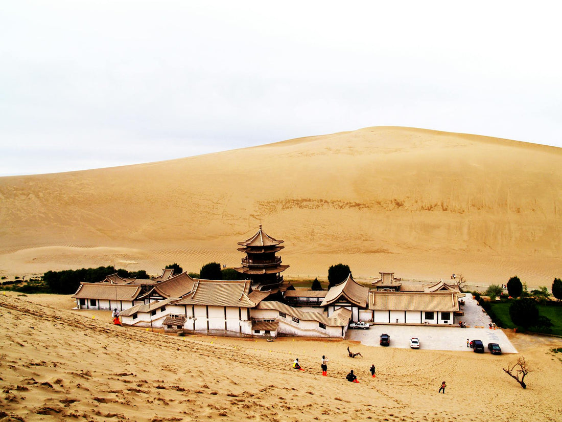 A scenic view of a temple at Echoing-Sand Mountain, Dunhuang, surrounded by desert sand dunes.